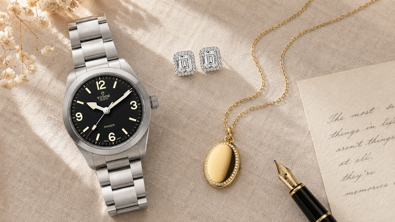 A specialist presenting three beige velvet jewelry boxes containing a diamond solitaire necklace, diamond studs, and a diamond ring.