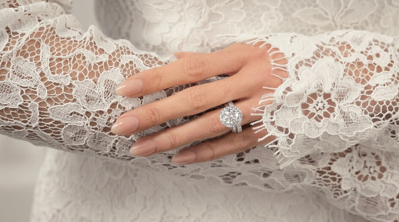 A close up of a hand wearing a diamond engagement ring stacked with a matching wedding band to illustrate how they differ in design and purpose